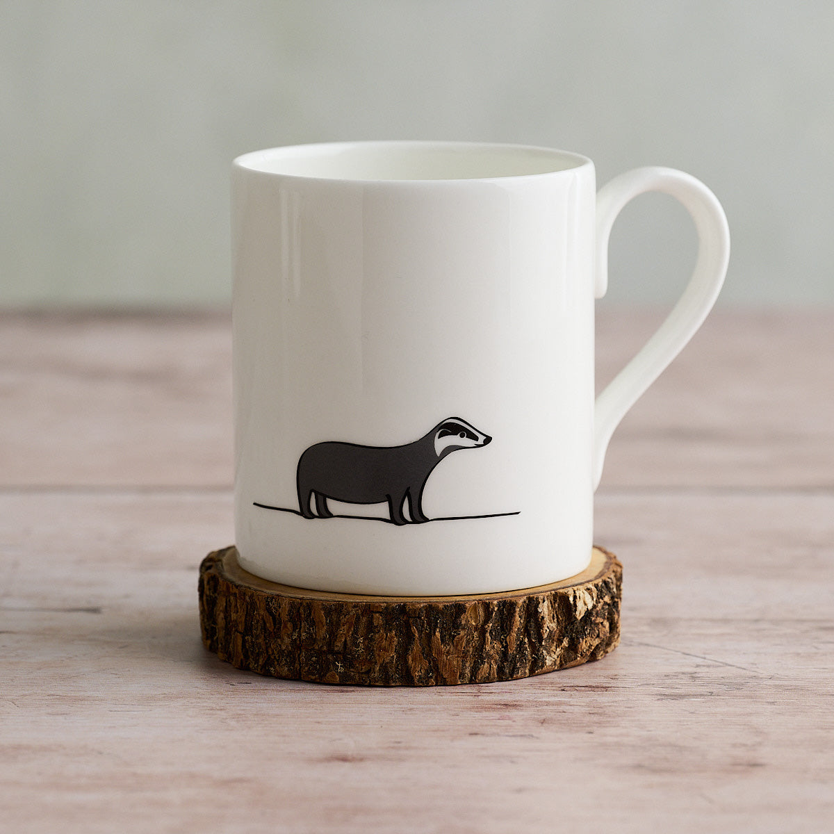 White mug with a Badger illustration on a wooden coaster