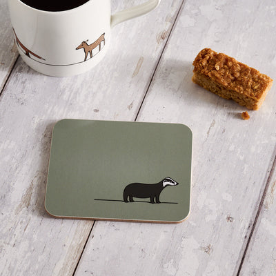 Coaster with badger design on a wooden surface with a mug and snack.