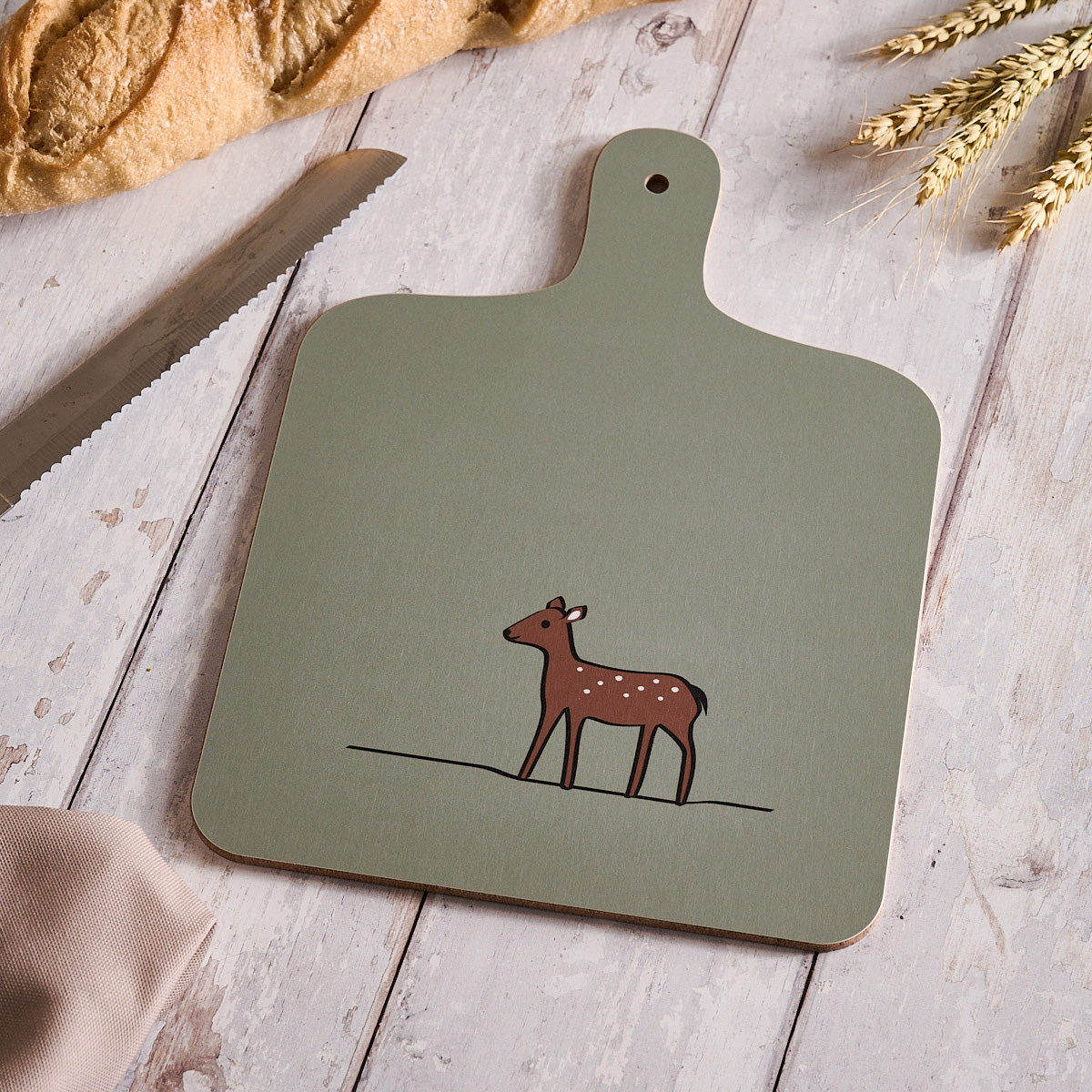 Soft Sage Green Chopping Board with a deer illustration on a wooden surface with bread and wheat.