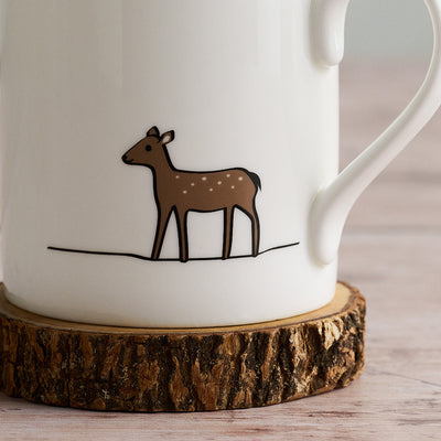 White mug with a brown Deer illustration on a wooden coaster