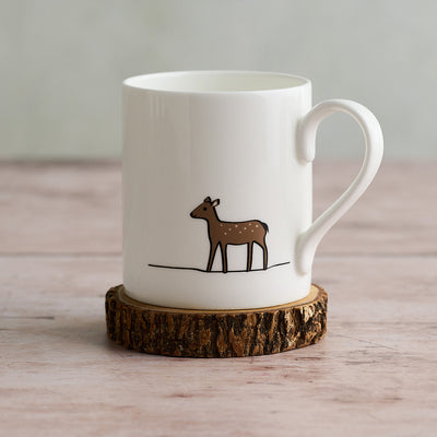 White mug with a deer illustration on a wooden coaster
