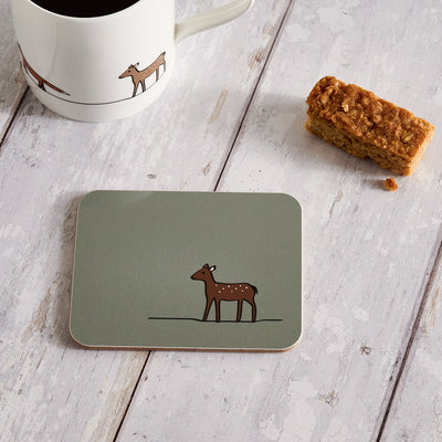 Coaster with deer design on a wooden surface with a mug and snack.