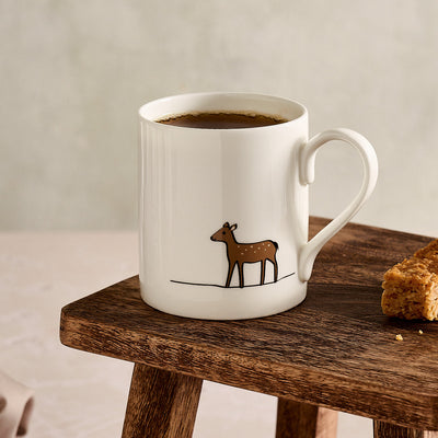 White mug with a deer design on a wooden table with a light background
