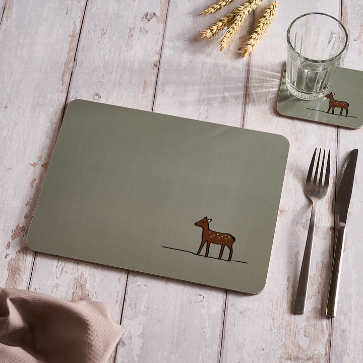 Sage Green placemat with a deer design on a wooden table with cutlery and a glass.
