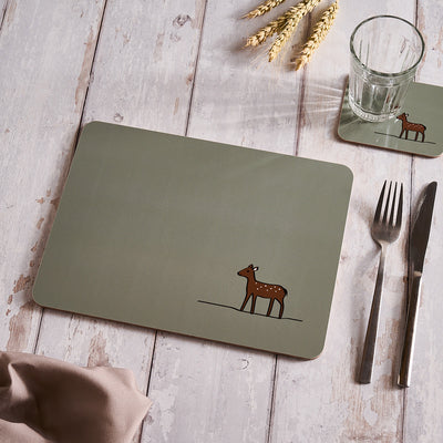 Sage Green placemat with a deer design on a wooden table with cutlery and a glass.