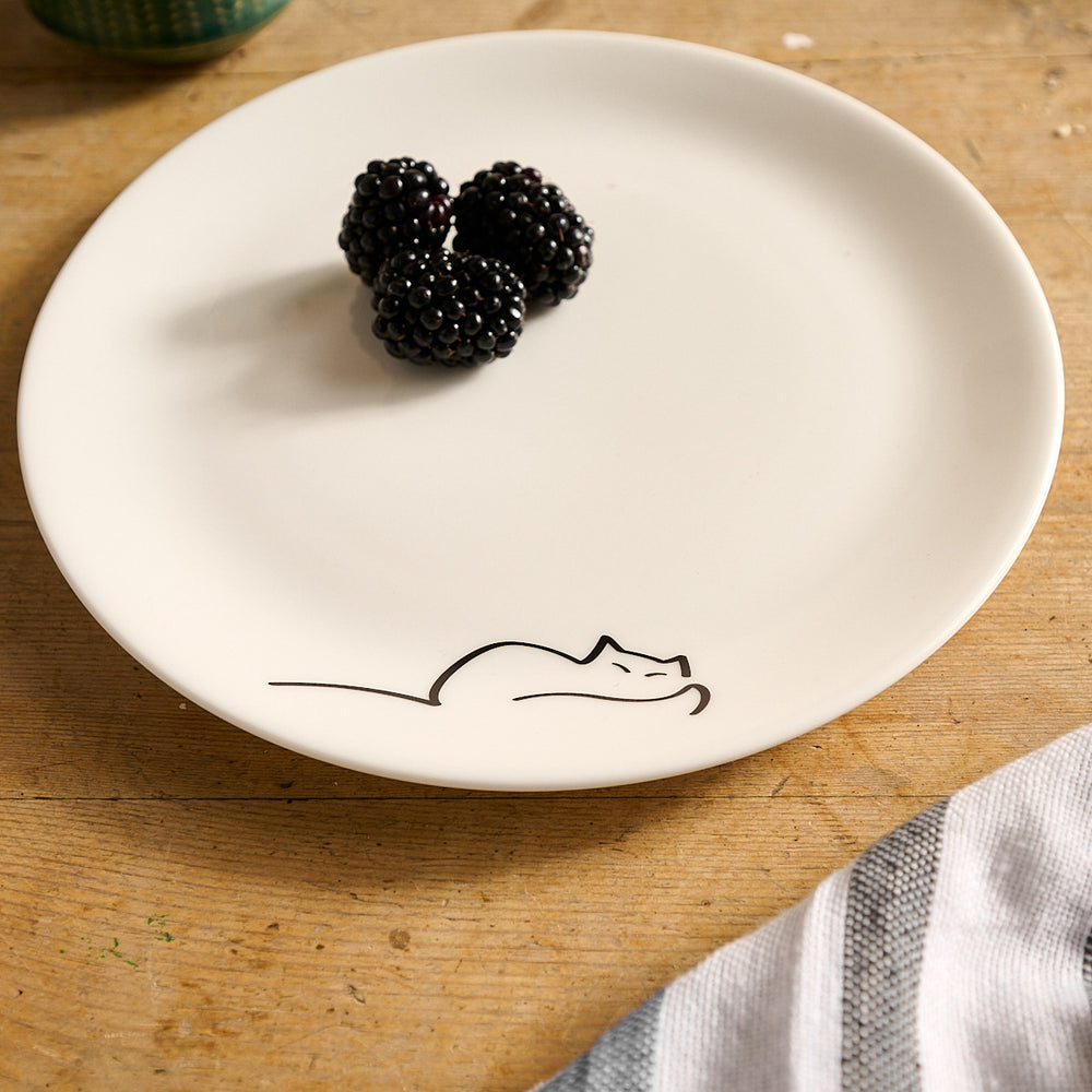 Dreaming Cat Side Plate with a black line drawing of a cat and two blackberries on a wooden surface.