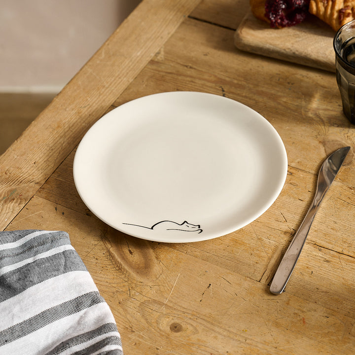Dreaming Cat Side Plate with a black outline cat design on a wooden table with a knife and napkin.
