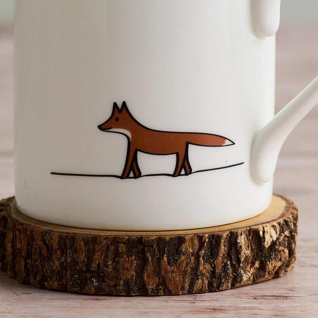 White mug with a brown fox illustration on a wooden coaster