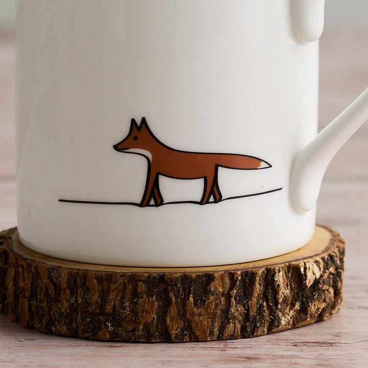 White mug with a brown fox illustration on a wooden coaster