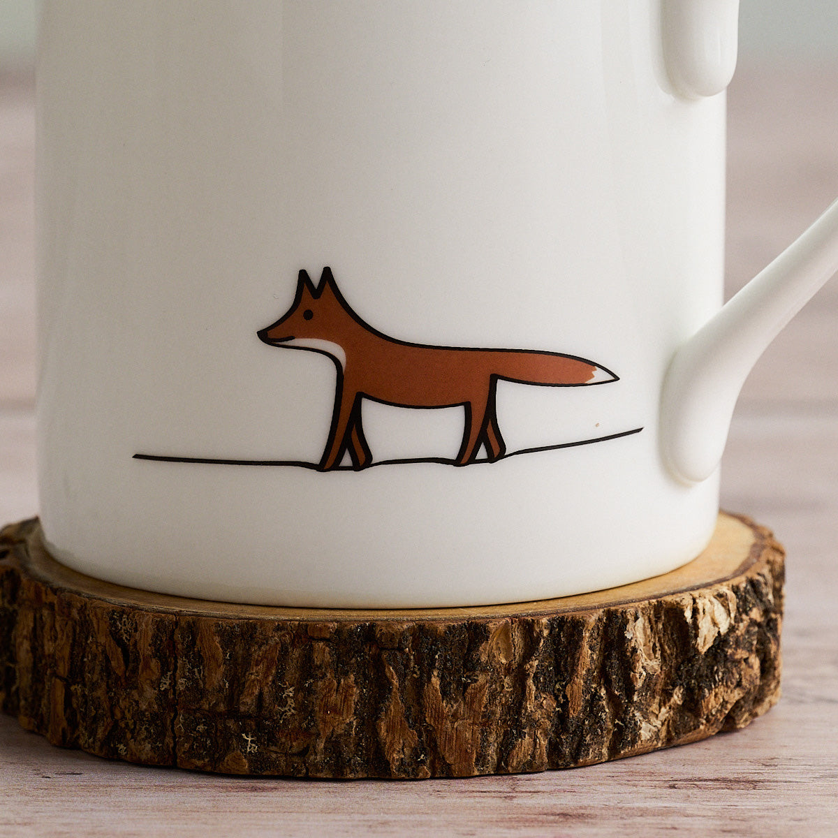 White mug with a brown fox illustration on a wooden coaster