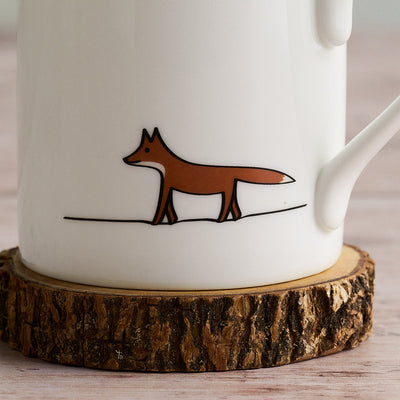 White mug with a brown fox illustration on a wooden coaster