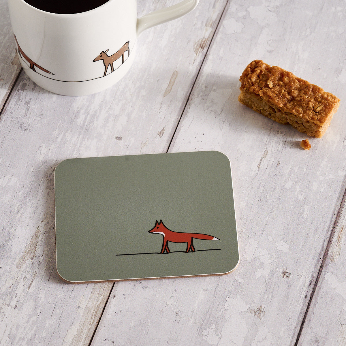 Coaster with fox design on a wooden surface with a mug and snack.
