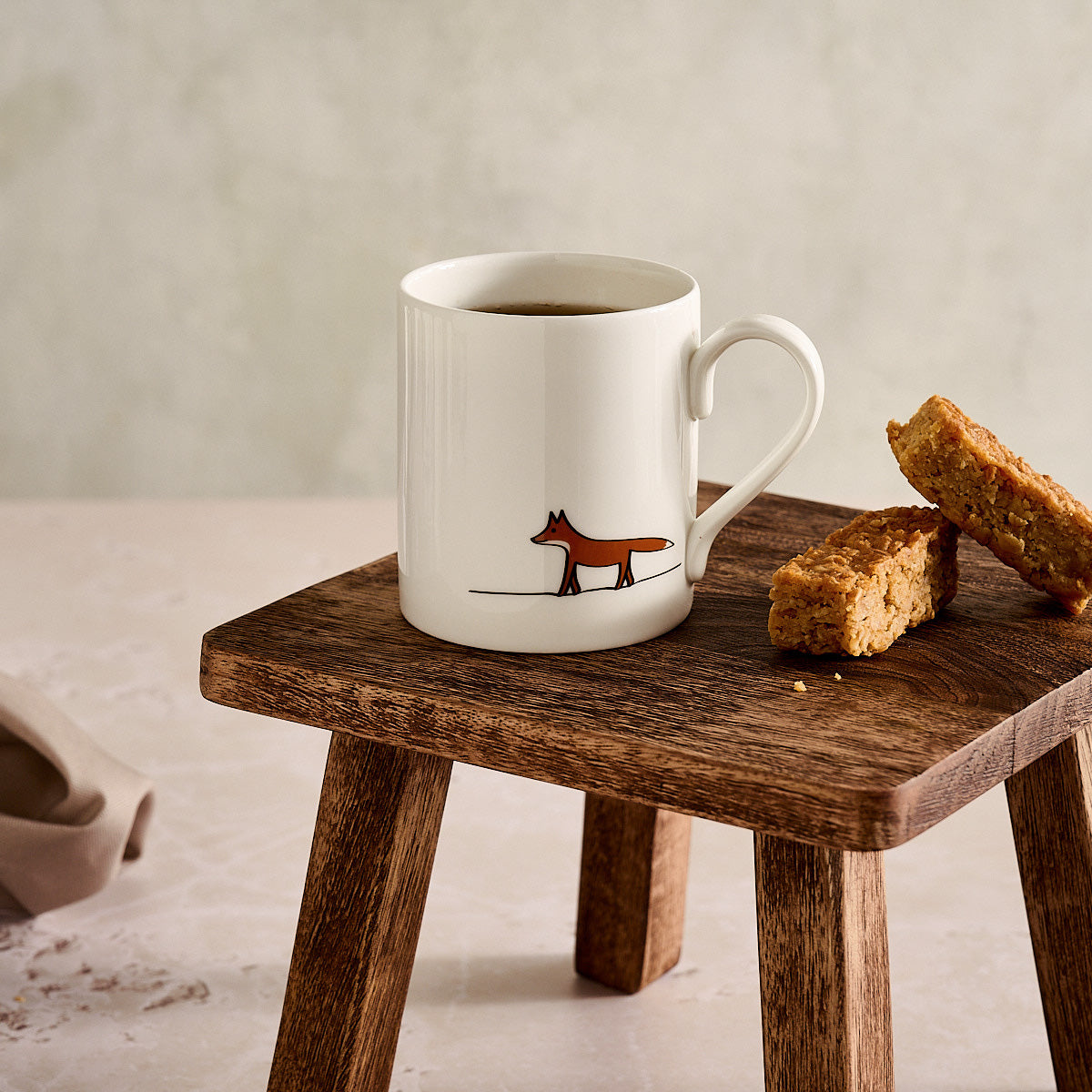 White mug with a fox design on a wooden stool with flapjacks