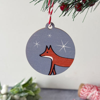 Round Christmas ornament with a fox design hanging from a tree.