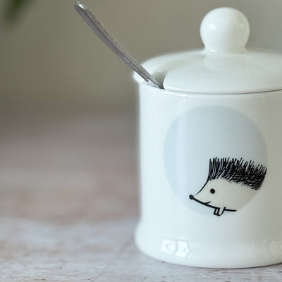 White fine bone china jam pot with a hedgehog design and a spoon inside, on a wooden surface