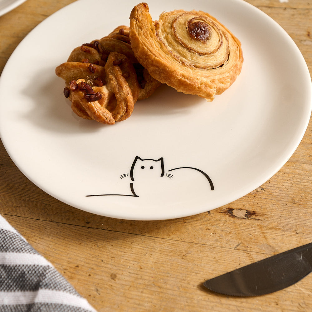 Two pastries on Loafing Cat Side plate with a cat illustration on a wooden surface.