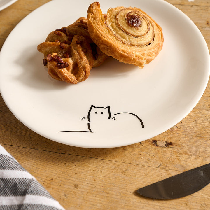 Two pastries on Loafing Cat Side plate with a cat illustration on a wooden surface.