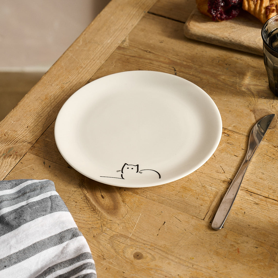 Loafing Cat Side Plate on a wooden table with a knife and striped cloth.