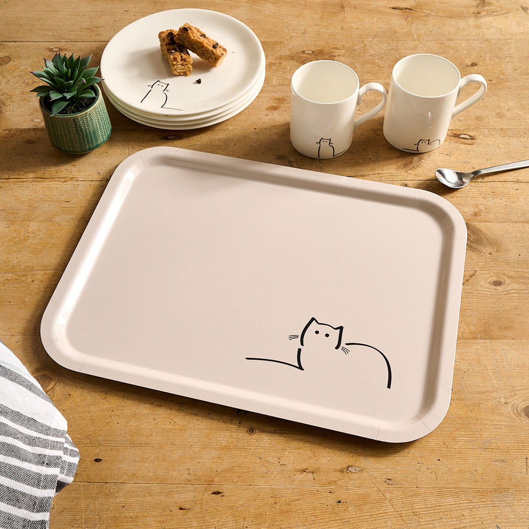 Light cream tray with Loafing Cat on a wooden table with mugs and plates.