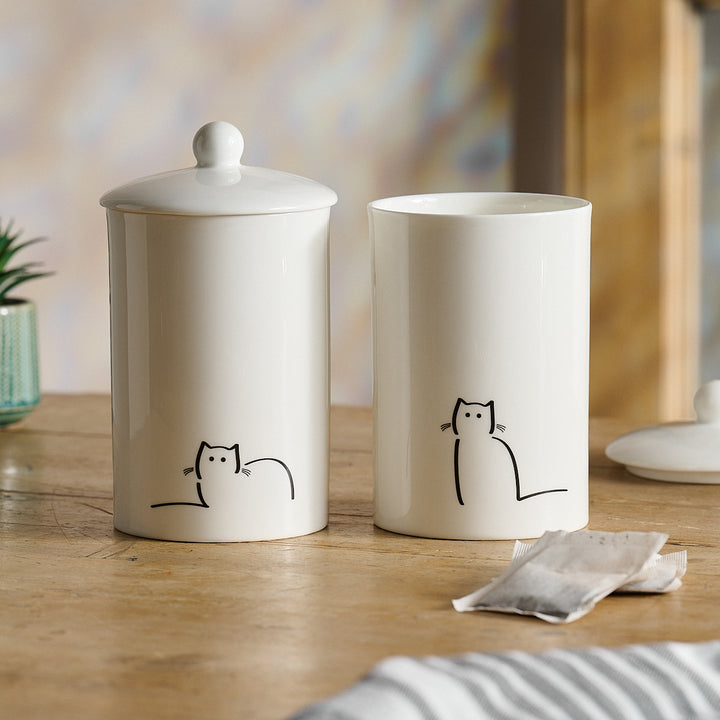 Two white storage jars with cat illustrations on a wooden surface.