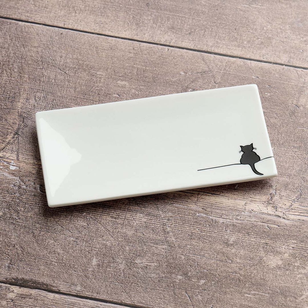 A rectangular glossy white ceramic dish with a small black cat silhouette sitting on a thin line near the bottom right, displayed on a rustic brown wooden surface.