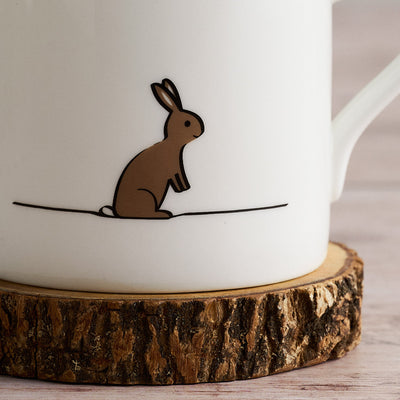 White mug with a brown rabbit illustration on a wooden coaster