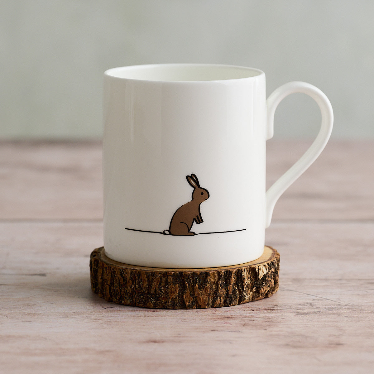 White mug with a rabbit illustration on a wooden coaster
