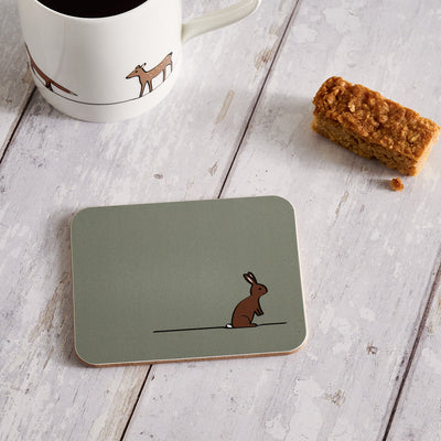 Coaster with a rabbit design on a wooden surface with a mug and snack.