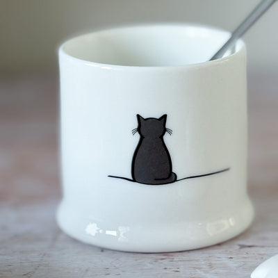 White fine bone china jam pot with a black cat illustration on a wooden surface