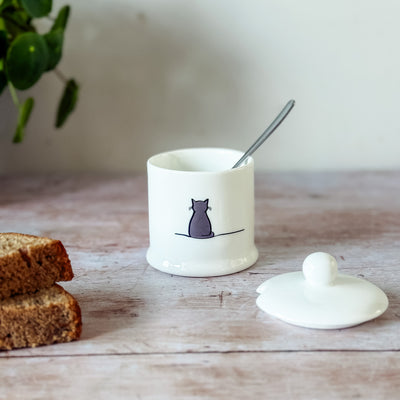 White fine bone china jam pot with Sitting Cat design, spoon, and bread on a wooden surface.