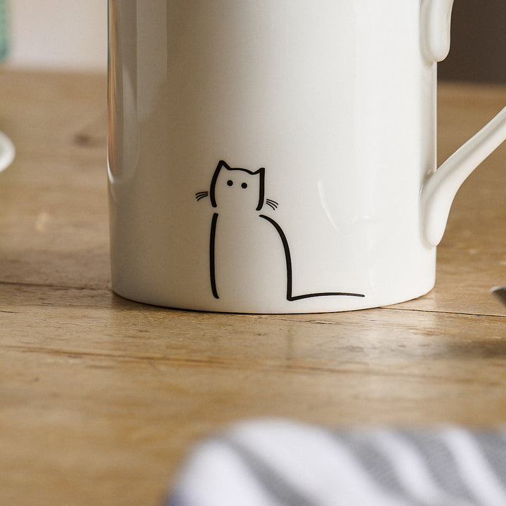 Waiting Cat White mug close up with a black cat illustration on a wooden surface