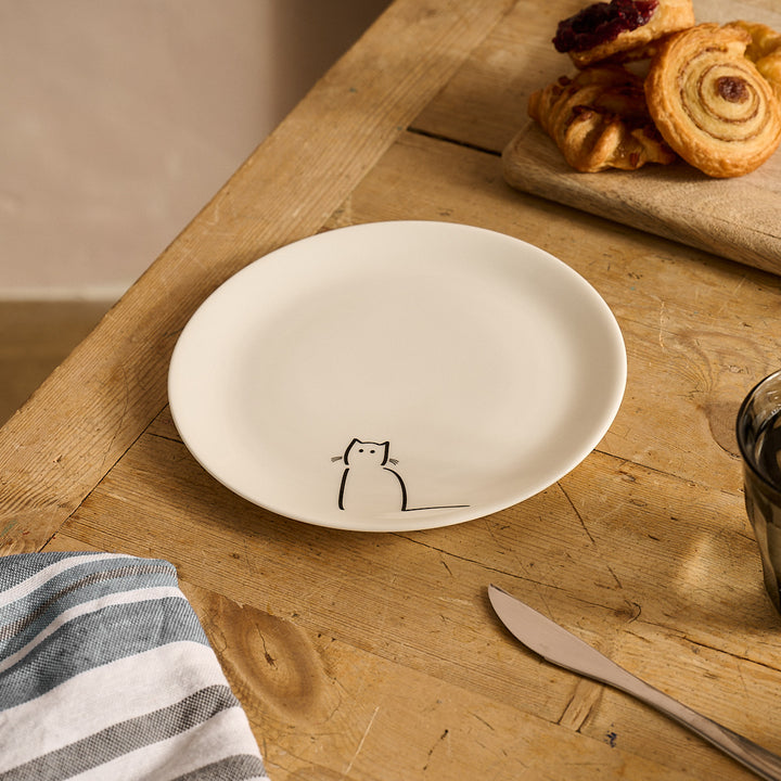 Waiting Cat Side Plate on a wooden table with pastries and a knife.