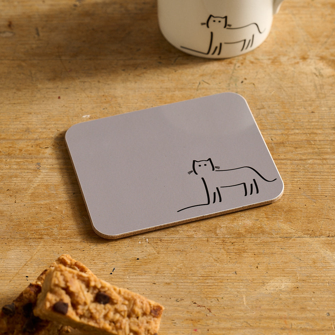 Watching Cat Coaster with cat design on a wooden surface with a mug and cookies.