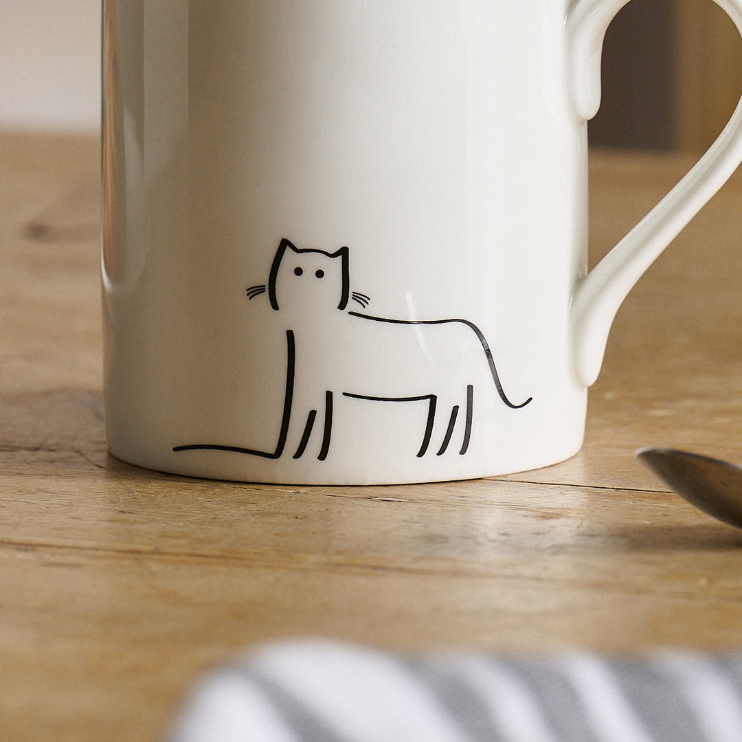 Watching Cat on a White mug with a black line drawing of a cat on a wooden surface
