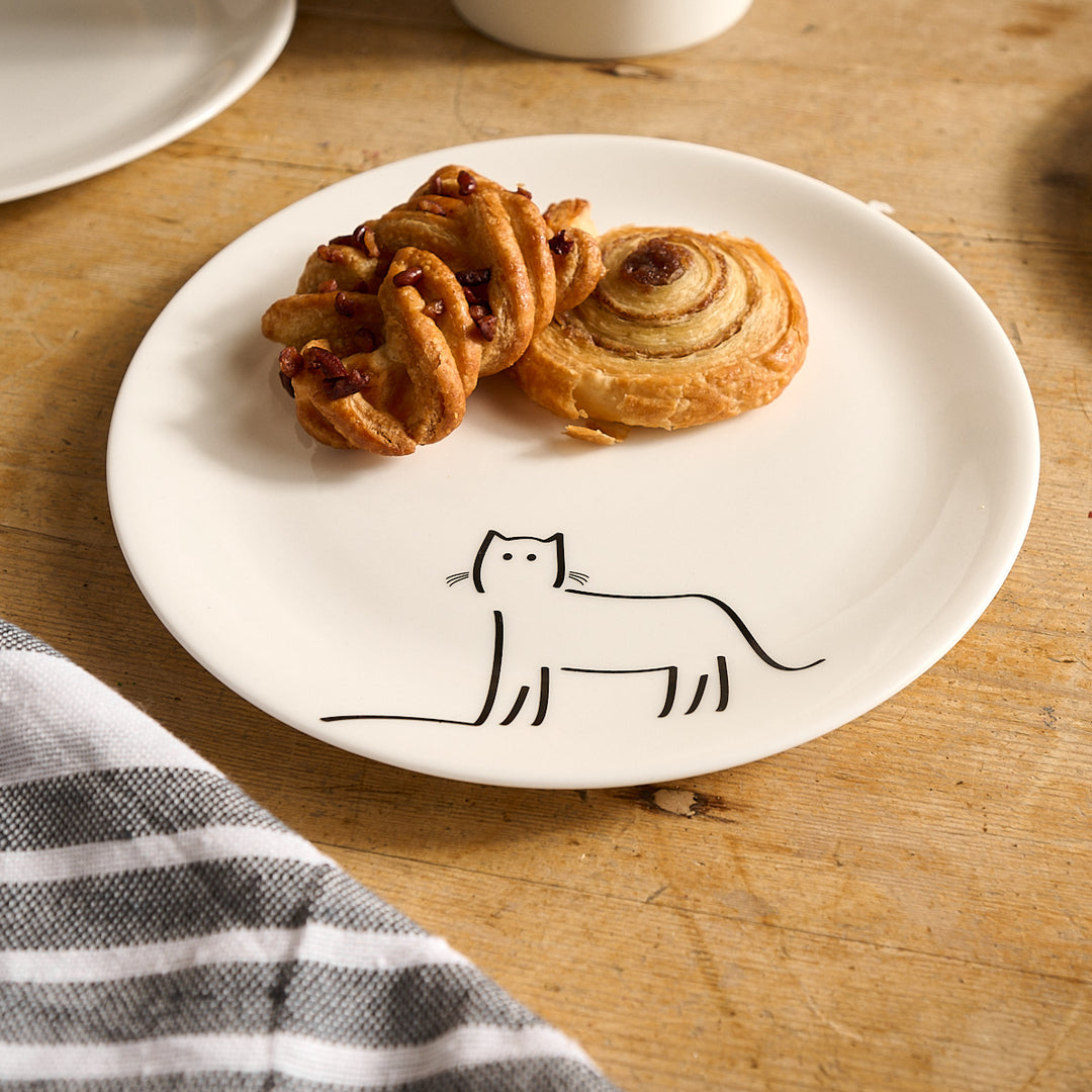 Watching Cat Side Plate with cat illustration and pastries on a wooden table