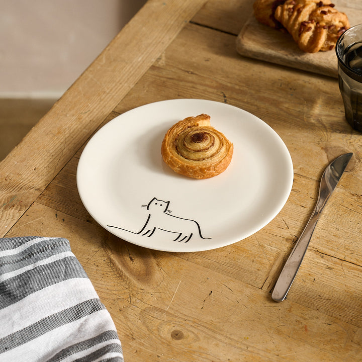 Watching Cat Side Plate with a cat illustration on a wooden table with a pastry and knife.