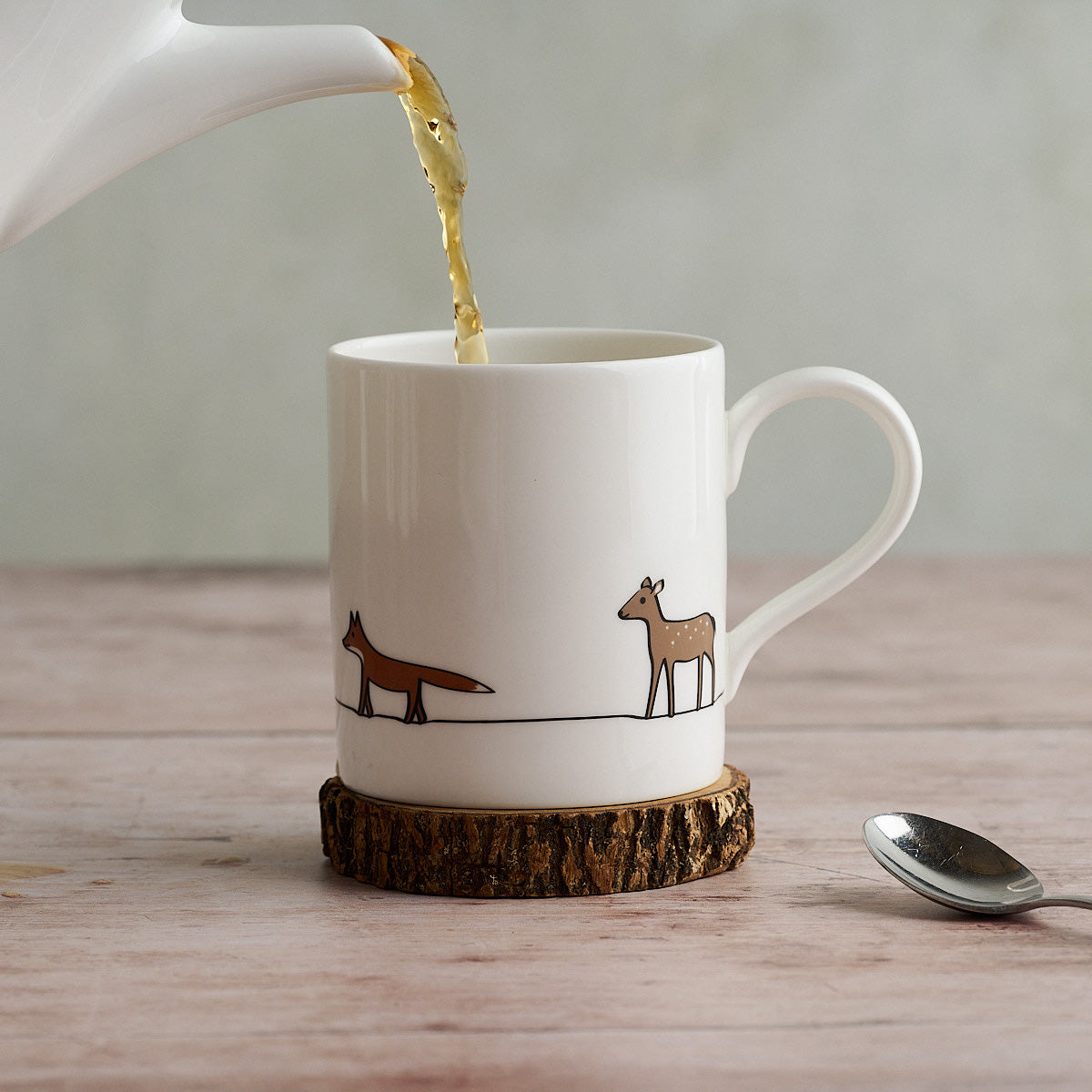 Tea being poured into a mug with Fox and Deer on a wooden coaster.