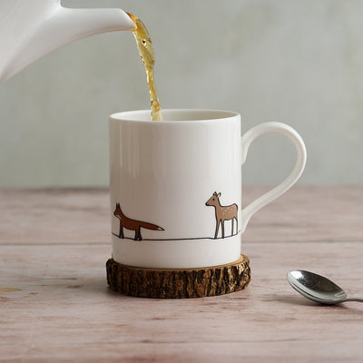 Tea being poured into a mug with Fox and Deer on a wooden coaster.