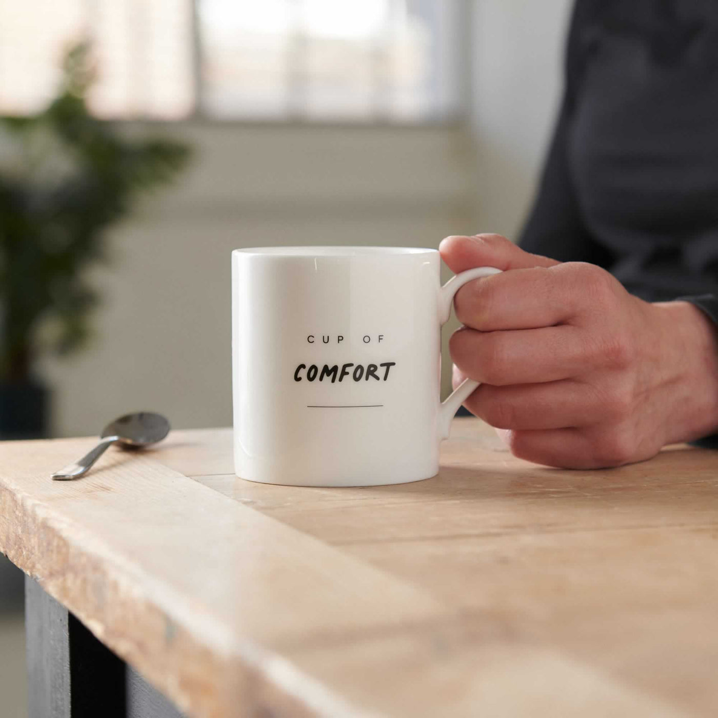 Cup of Comfort Mug on table with hand