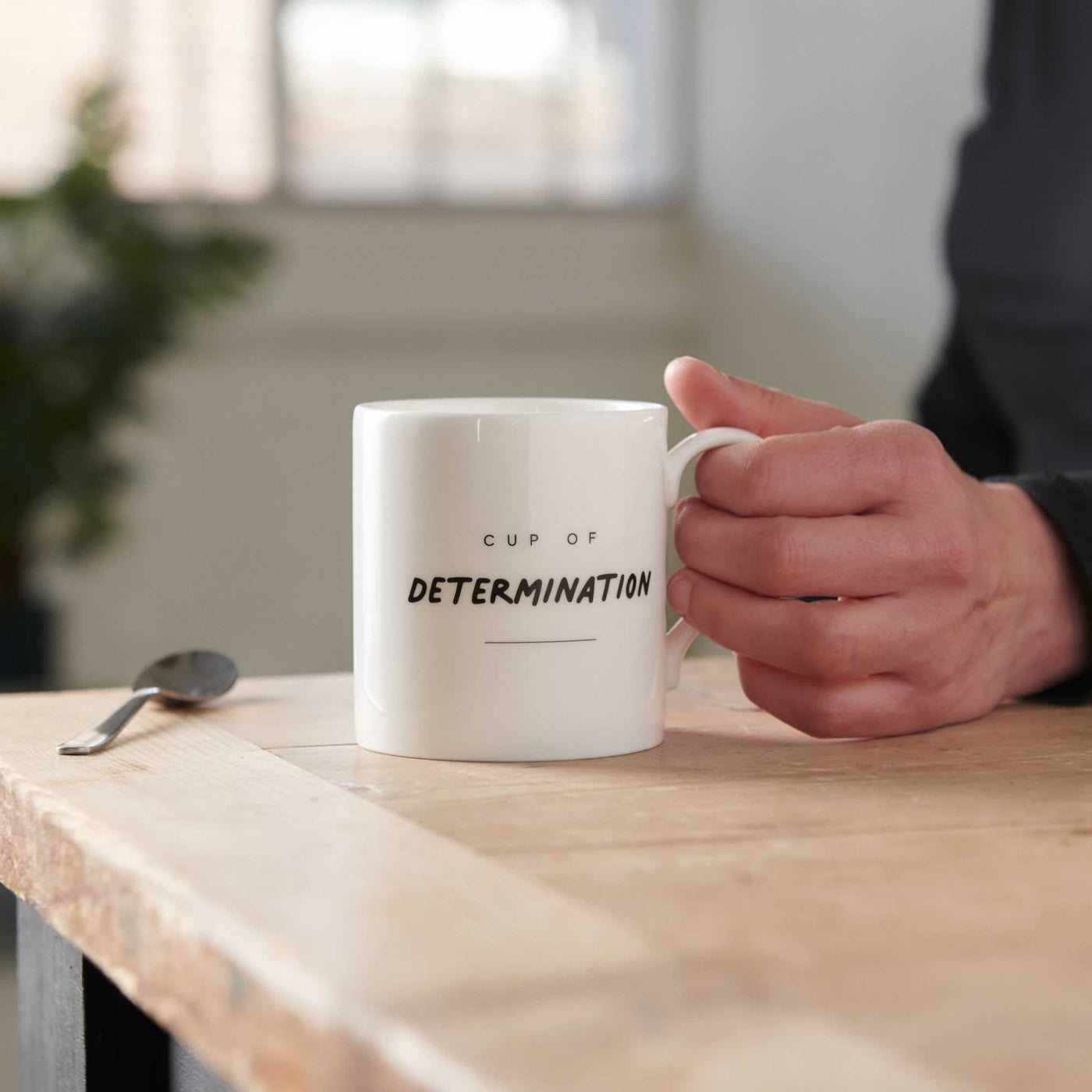 Cup of Determination Mug on table with hand