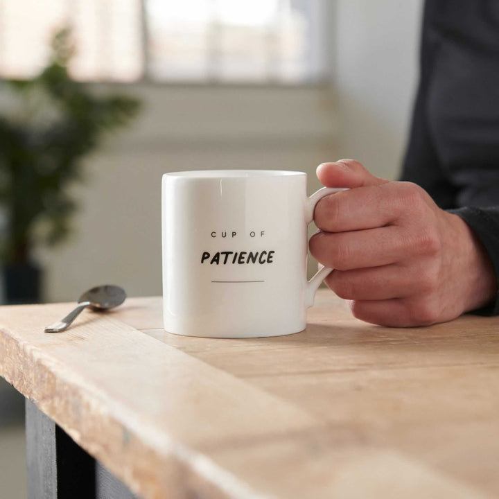 Cup of Patience Mug on table with hand